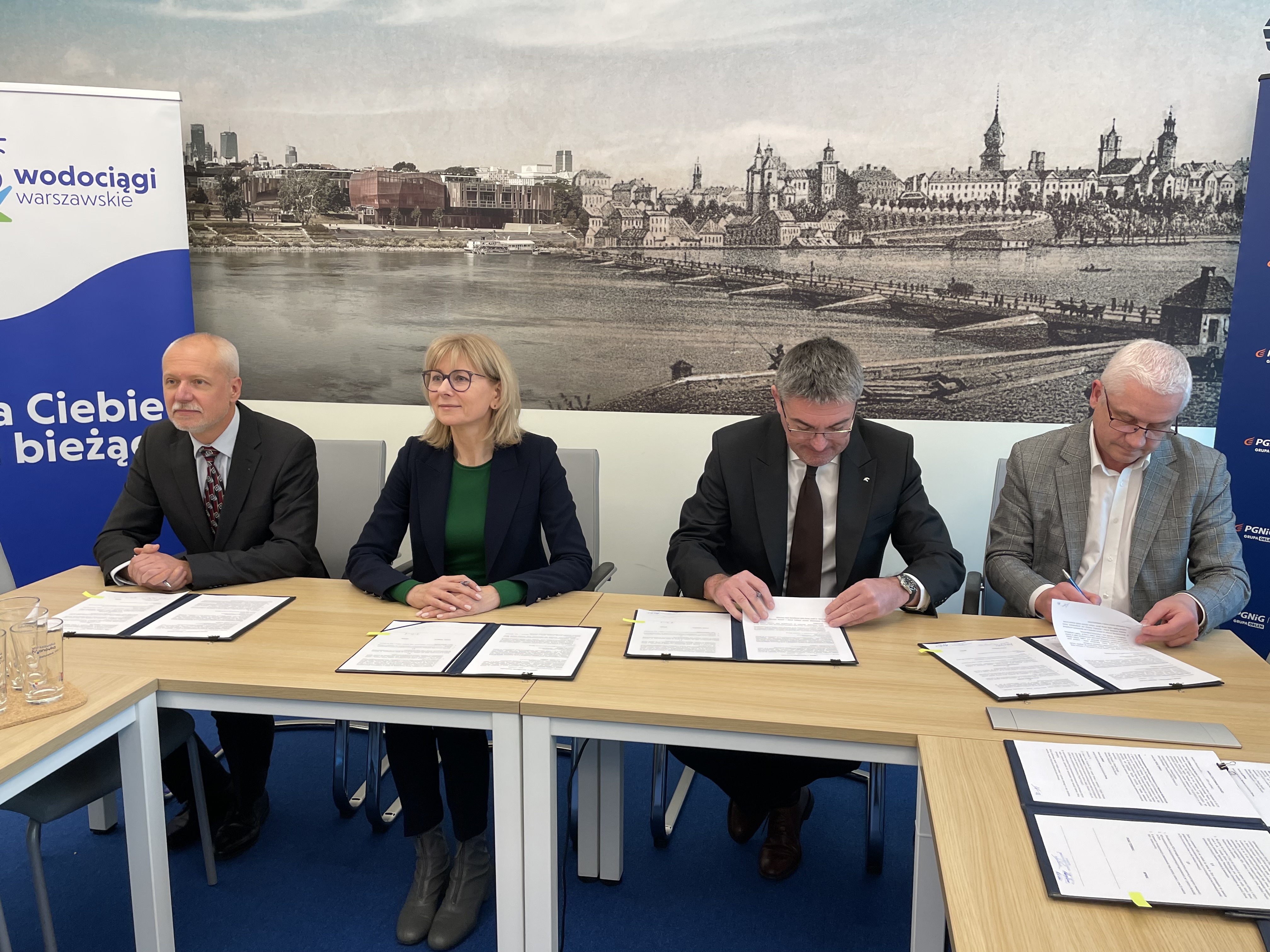 Przedstawiciele zarządu MPWiK oraz PGNiG Termika siedzą za stołem i podpisują dokumenty.