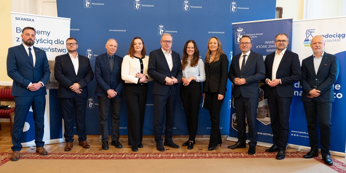 Grupa osób upranych oficjalnie pod ścianka z logo m.st. Warszawy.